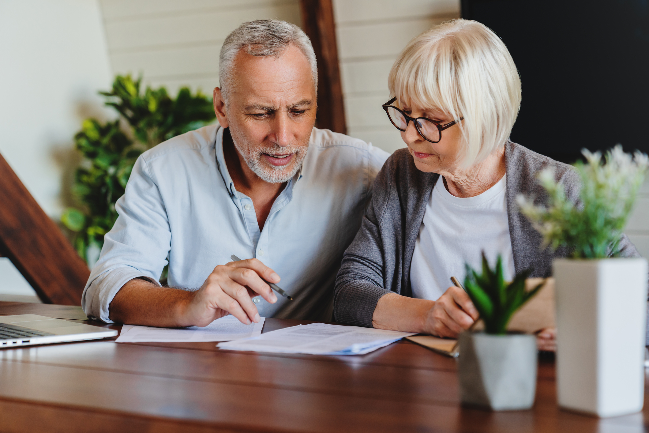 An older man and woman examine financial paperwork at their dinner table.