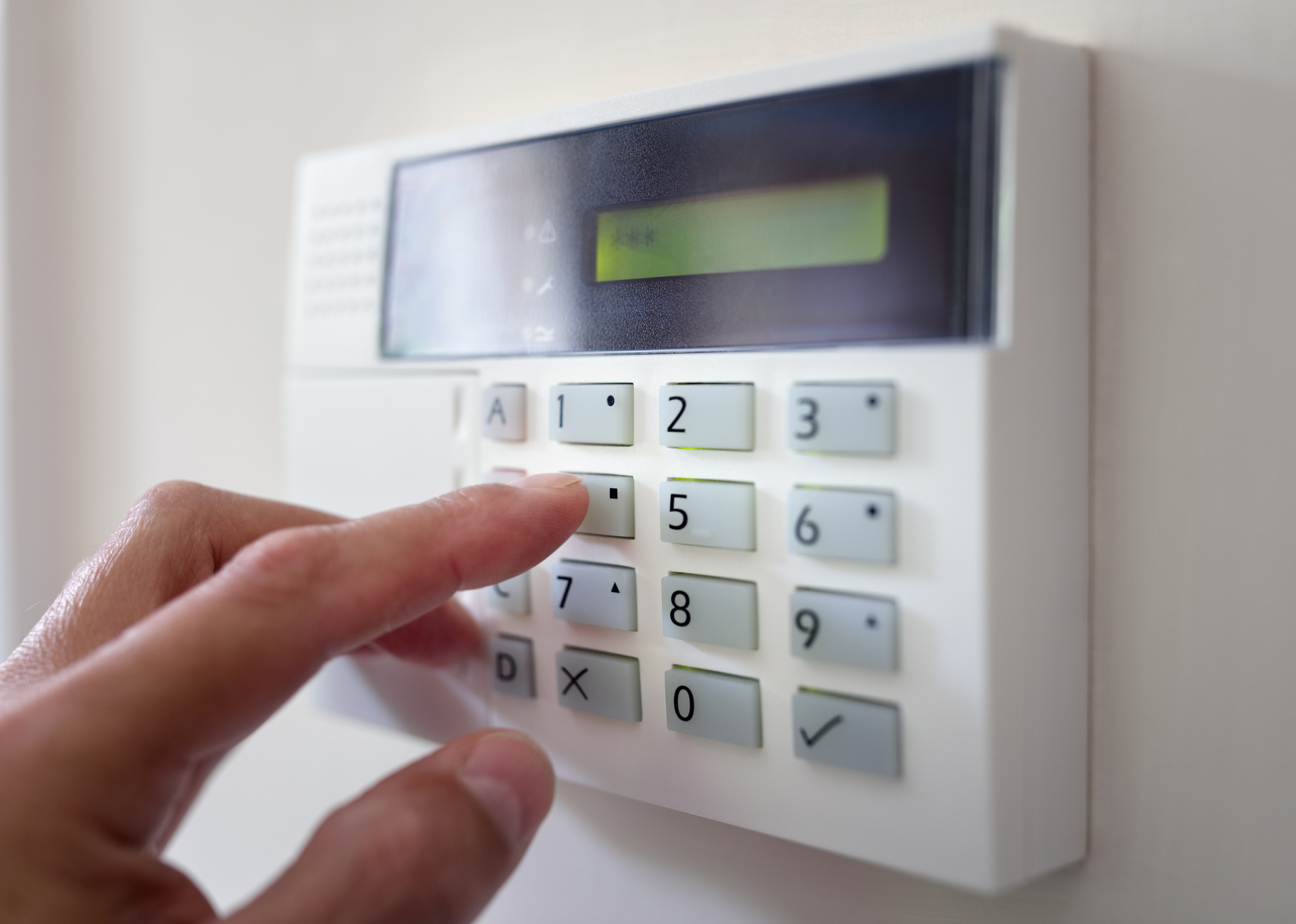 A closeup of someone’s hand setting the code for their home alarm system.